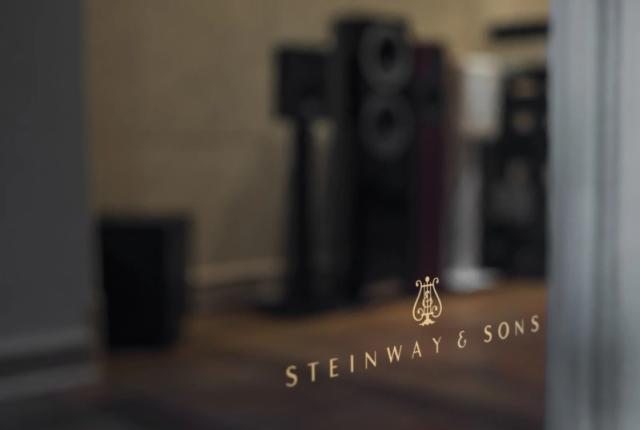 Логотип Steinway & Sons на чорній лакованій поверхні гучномовця, на якій відбиваються обриси інших гучномовців