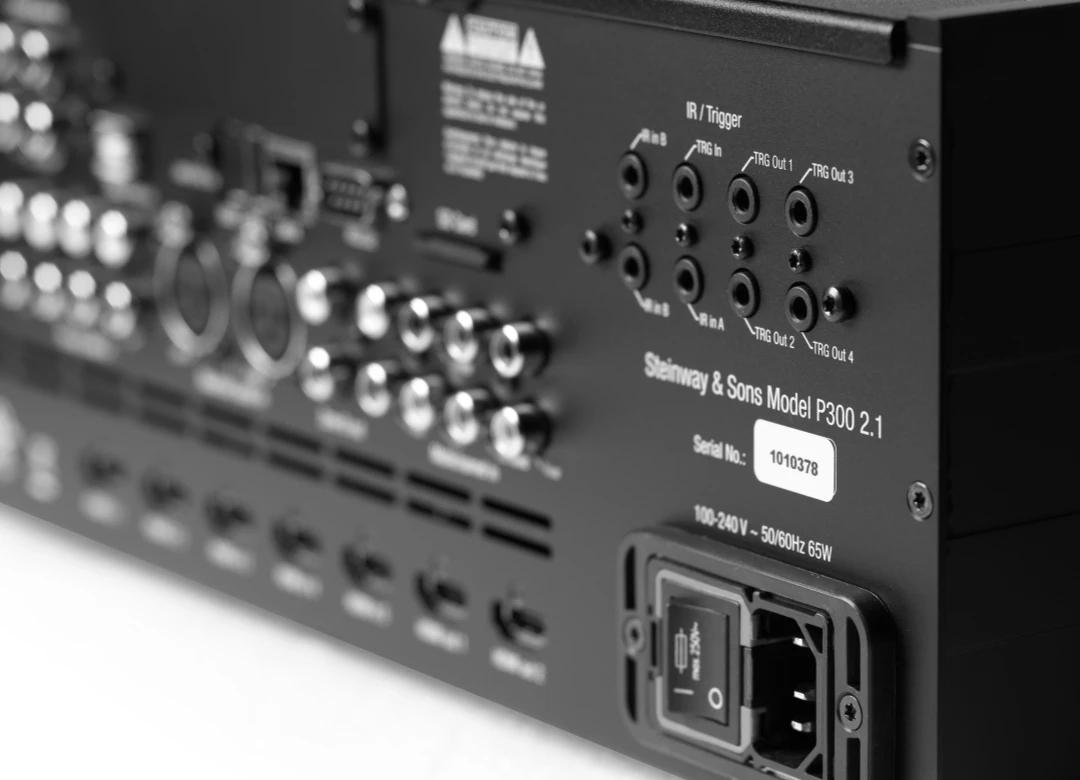  Великим планом задня панель багатоканального процесора Steinway & Sons P300 2.1, показана під кутом, із фокусом на ближній частині із назвою та гніздом живлення, основна частина панелі в розфокусованій зоні 