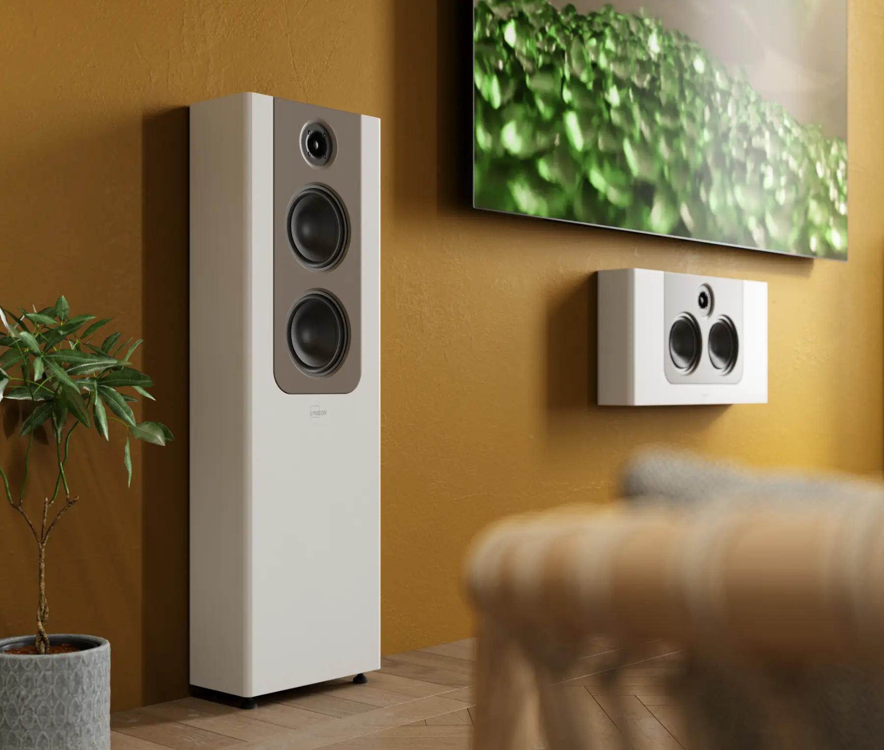 The Lyngdorf FR-2 and LCR-2 speakers are mounted on the wall; they have white cabinets with mocca panels, and part of a large television is visible, creating a striking contrast against the unusual colour of the wall