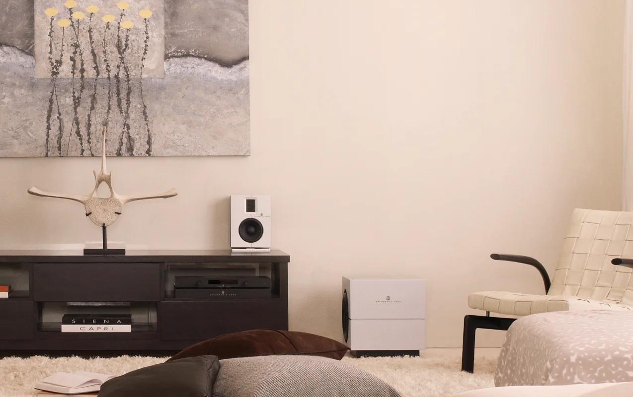 In the room, there is an SP-1 processor and an A-1 amplifier on a cabinet near the wall, a white Model S-15 loudspeaker, and a white Model S-210 woofer on the floor